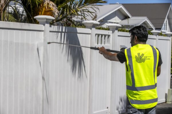 Kowhai Cleaning staff member water blasting white fence during exterior house washing in New Zealand