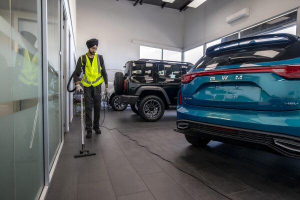 Commercial cleaning specialist vacuuming a car dealership showroom floor in New Zealand, part of professional interior cleaning and maintenance services.