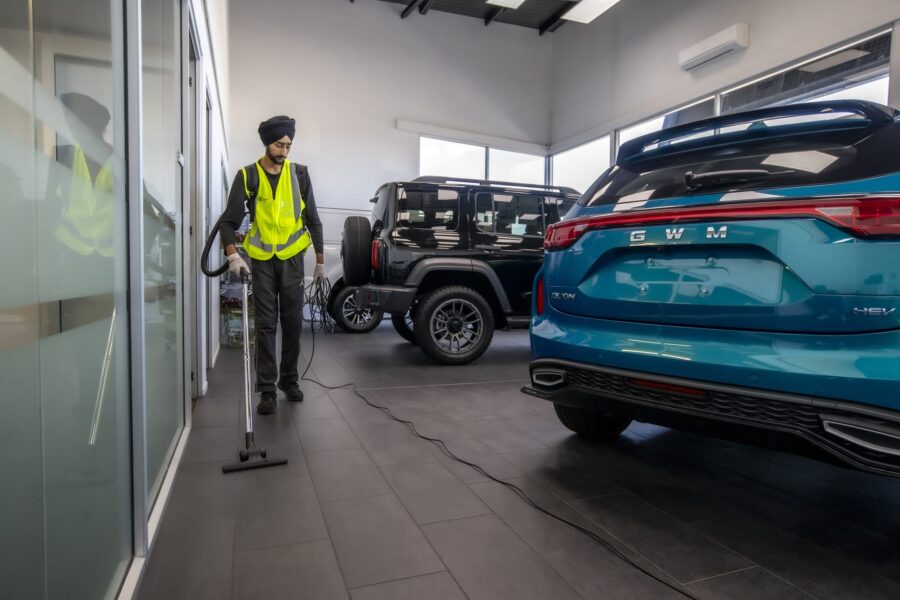 Commercial cleaning specialist vacuuming a car dealership showroom floor in New Zealand, part of professional interior cleaning and maintenance services.