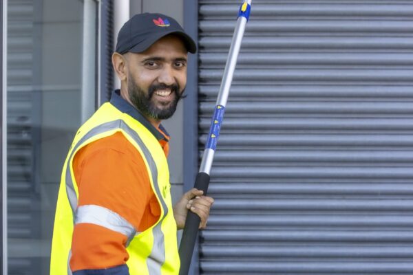 Exterior building cleaning technician using a telescopic wand to perform high-reach pressure washing on commercial property in Auckland, NZ.